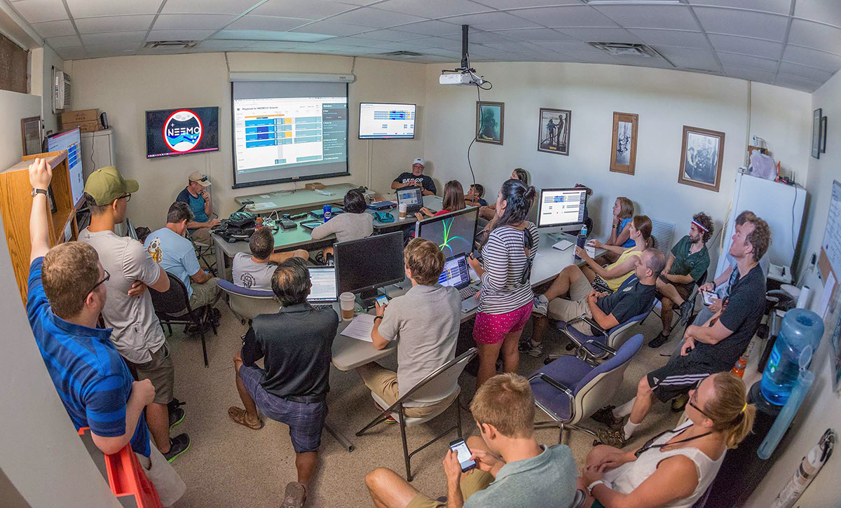 NASA Extreme Environment Mission Operations (NEEMO) mission control personnel gather to review the mission plan in Playbook
